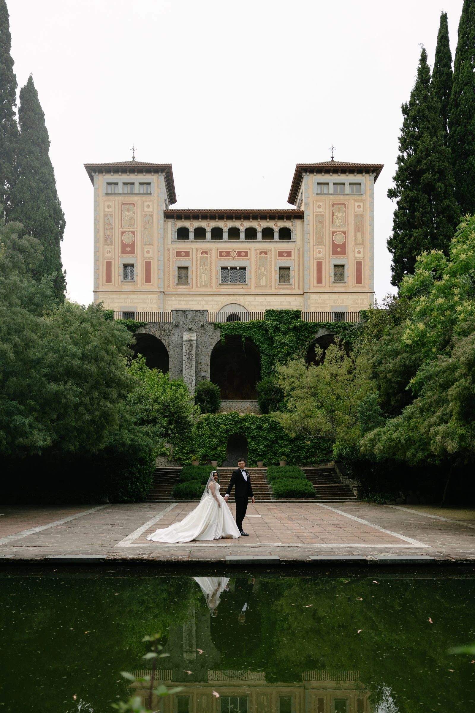 Los novios ante la fachada de Bell Recó, reflejada en el estanque del jardín