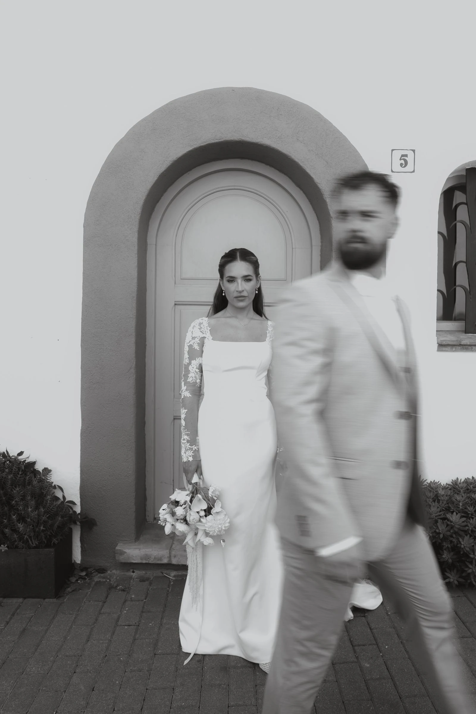Novios caminando junto a una puerta en arco, en blanco y negro