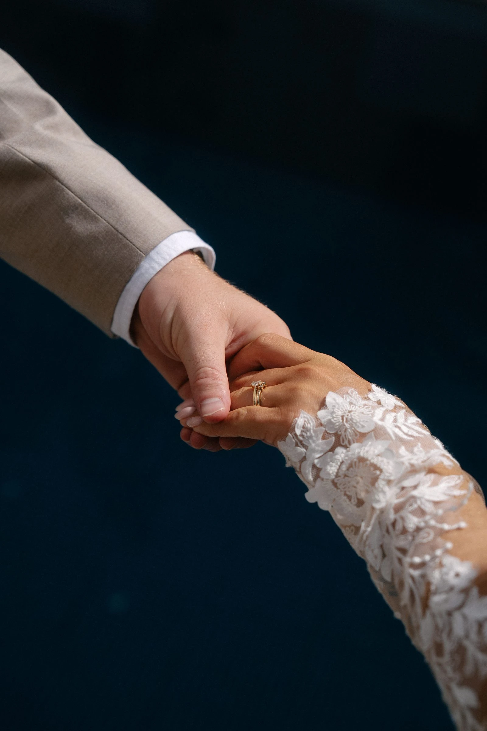 Manos de los novios entrelazadas sobre un fondo oscuro