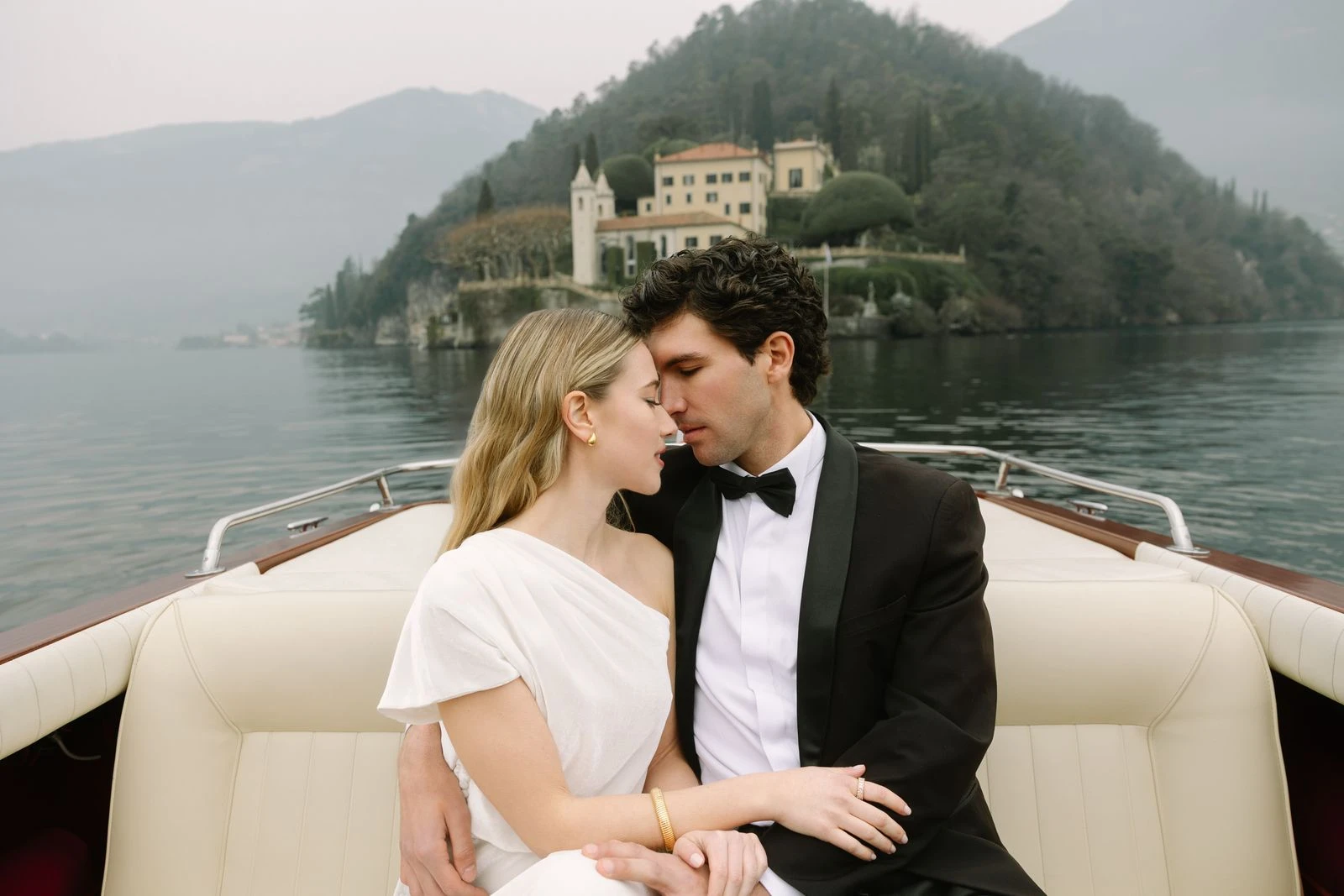 Novios besándose en la lancha con una isla al fondo